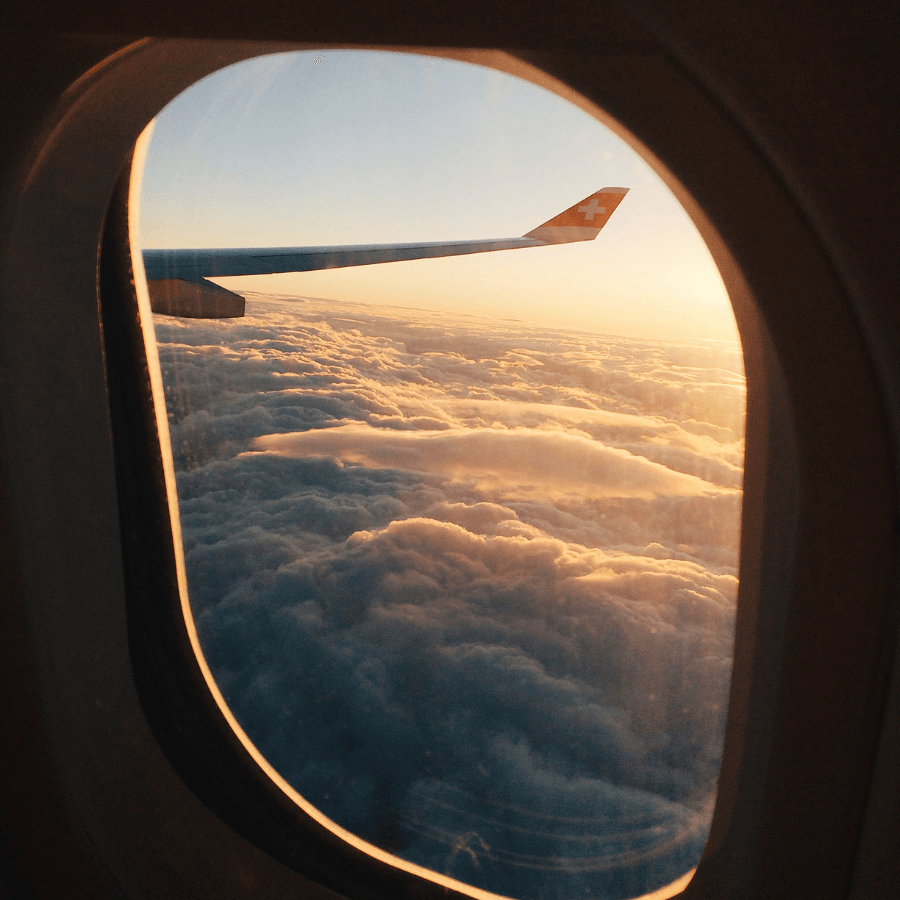 View of the sky from an airplane window. Sun is setting over clouds.