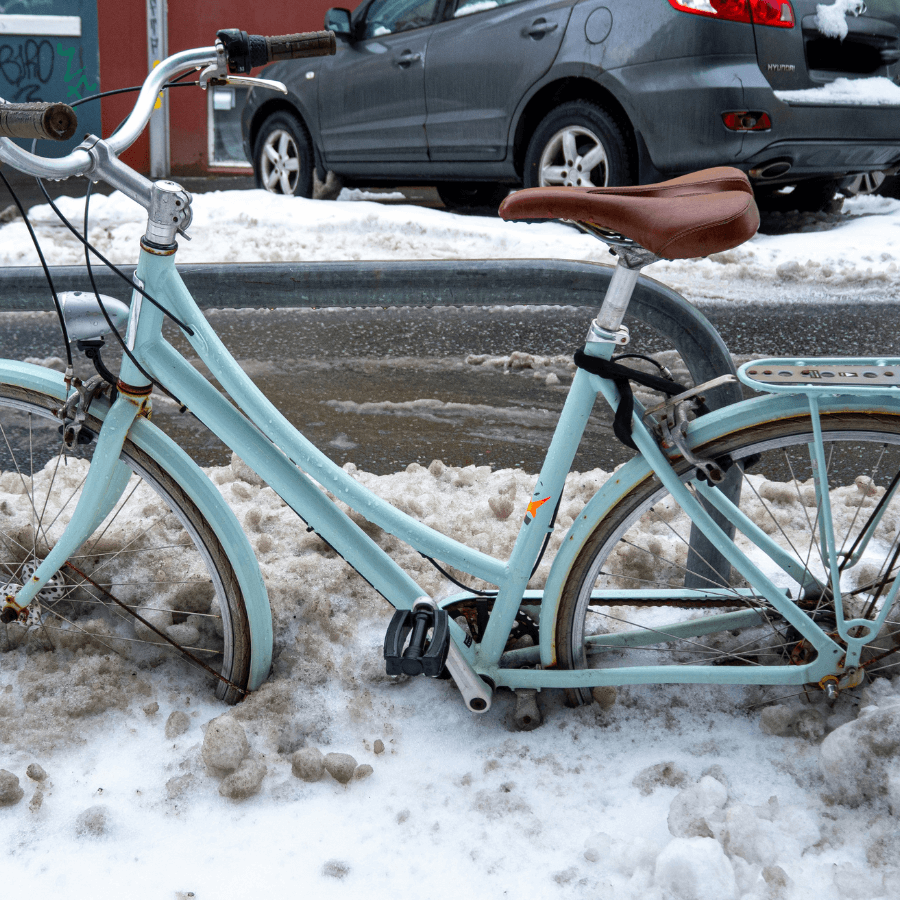 A blue bicycle stuck in the snow on the sidewalk