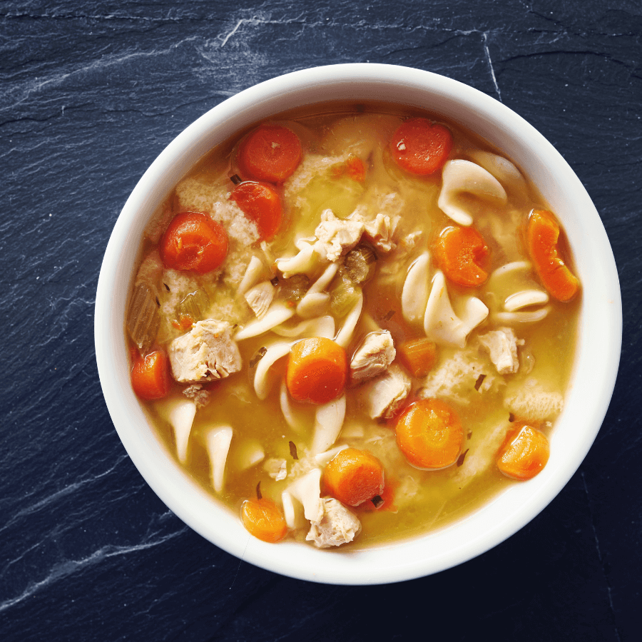 bowl of soup made with egg noodles, carrots, chicken and broth