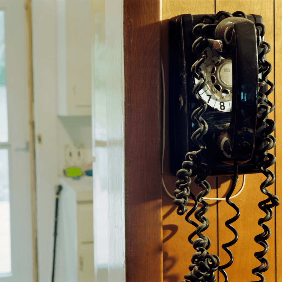An old dial telephone with a very long cord mounted on a wall in a kitchen